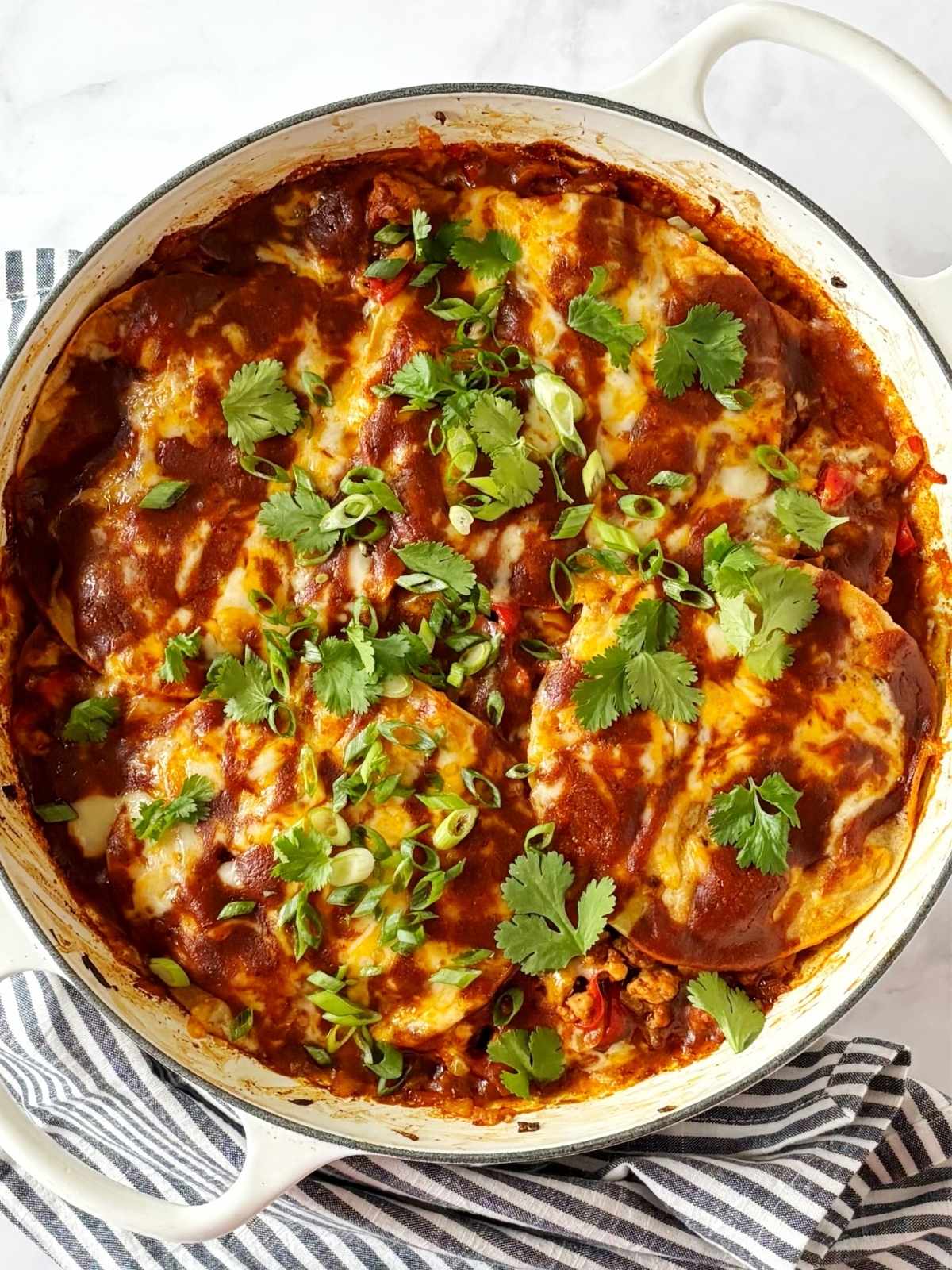 Ground turkey enchiladas in a skillet topped with scallions and cilantro for garnish.