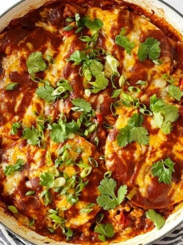 Turkey enchiladas with garnishes in a skillet.