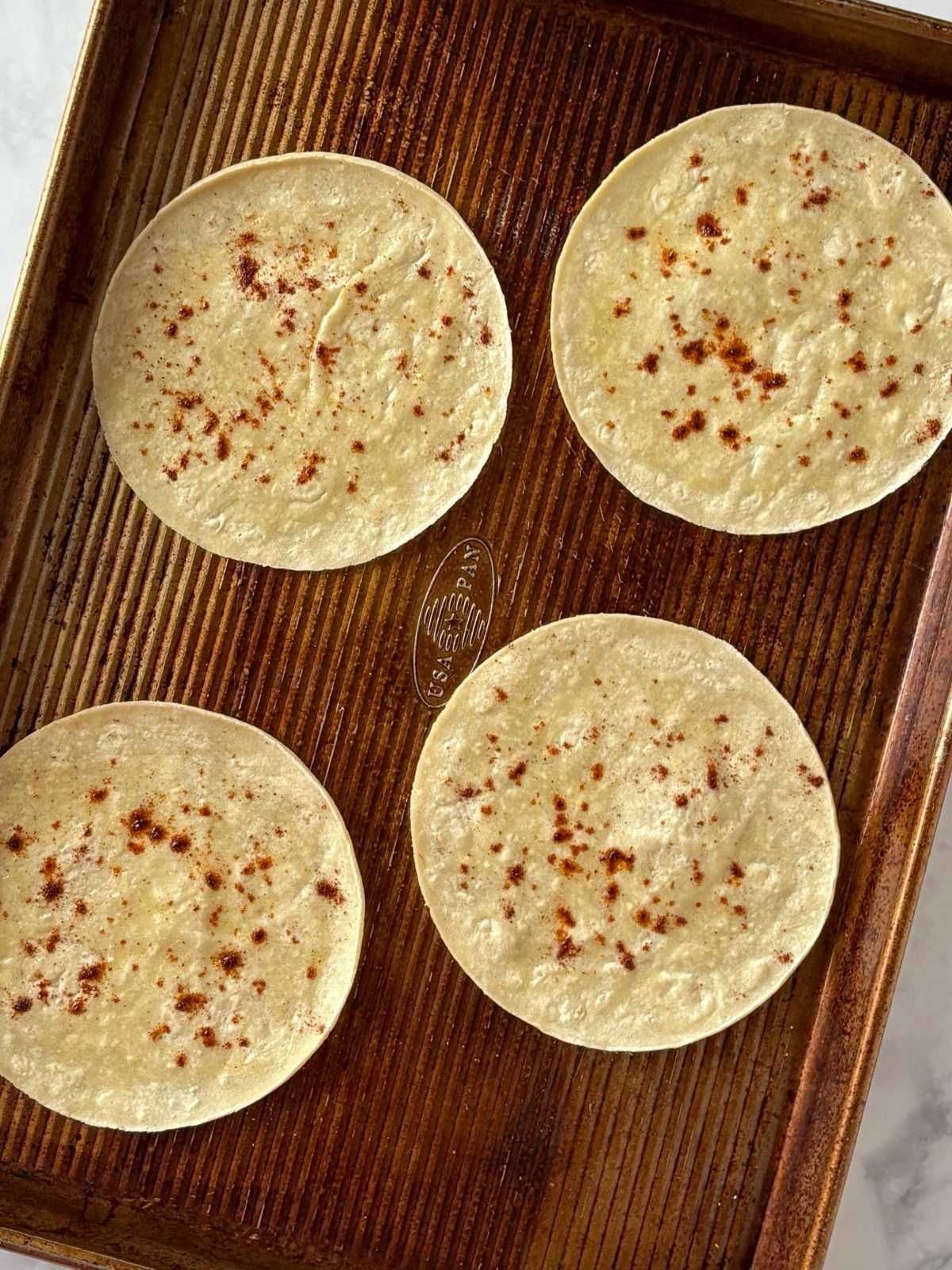 A sheet pan of tortillas brushed with oil and seasoned with chili powder.