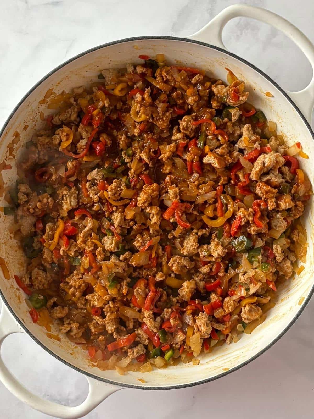 A skillet of veggies and turkey combined with enchilada sauce.