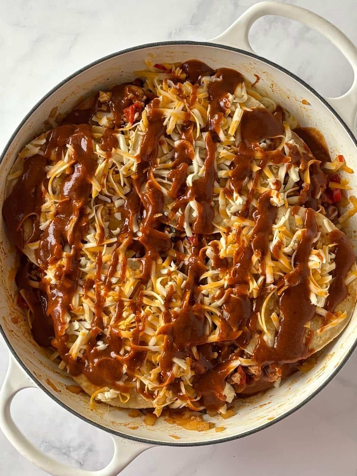 A skillet with two layers of turkey, tortillas, and cheese, topped with extra enchilada sauce.