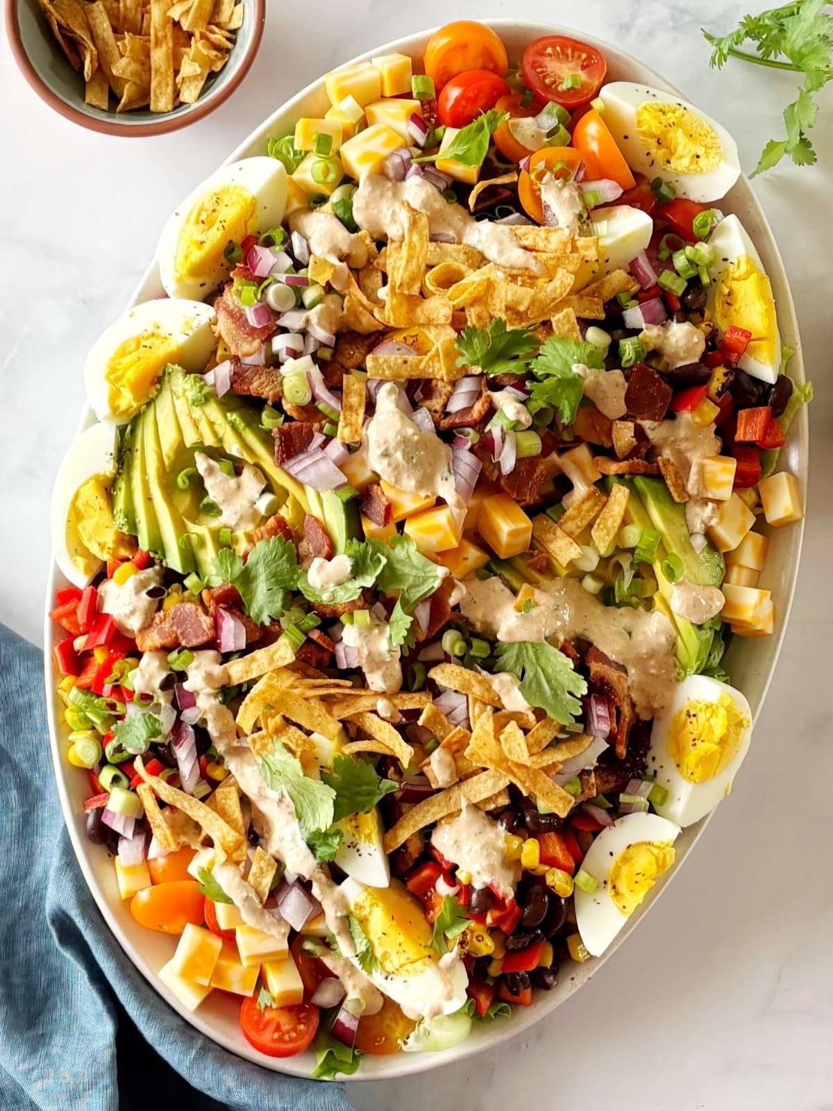 Mexican Cobb salad ingredients arranged on a platter and topped with dressing, cilantro, and tortilla strips.