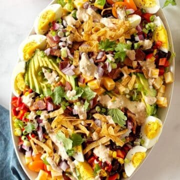 A serving platter of Mexican Cobb salad topped with dressing and garnishes.