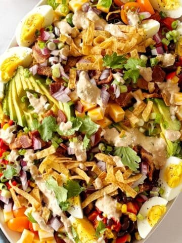 A serving platter of Mexican Cobb salad topped with dressing and garnishes.