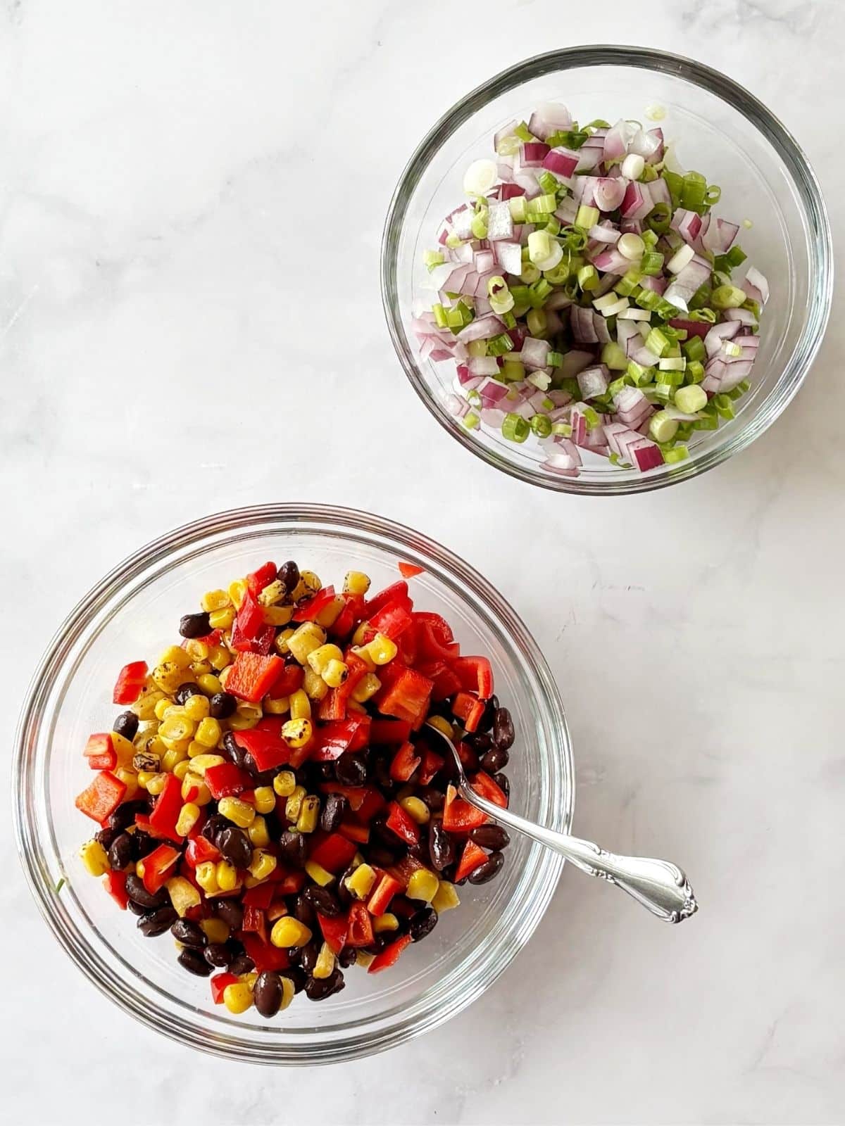 Red onions and scallions tossed in one bowl and red pepper, black beans, and corn in another.