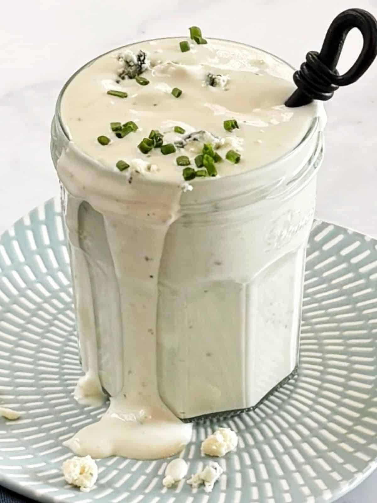 A glass jar filled with blue cheese dressing and garnished with chives.