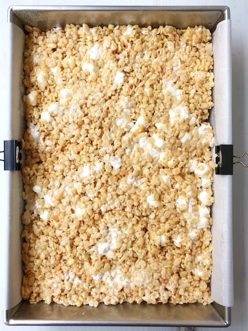 Cereal and marshmallow mixture pressed into a baking pan liined with parchment.