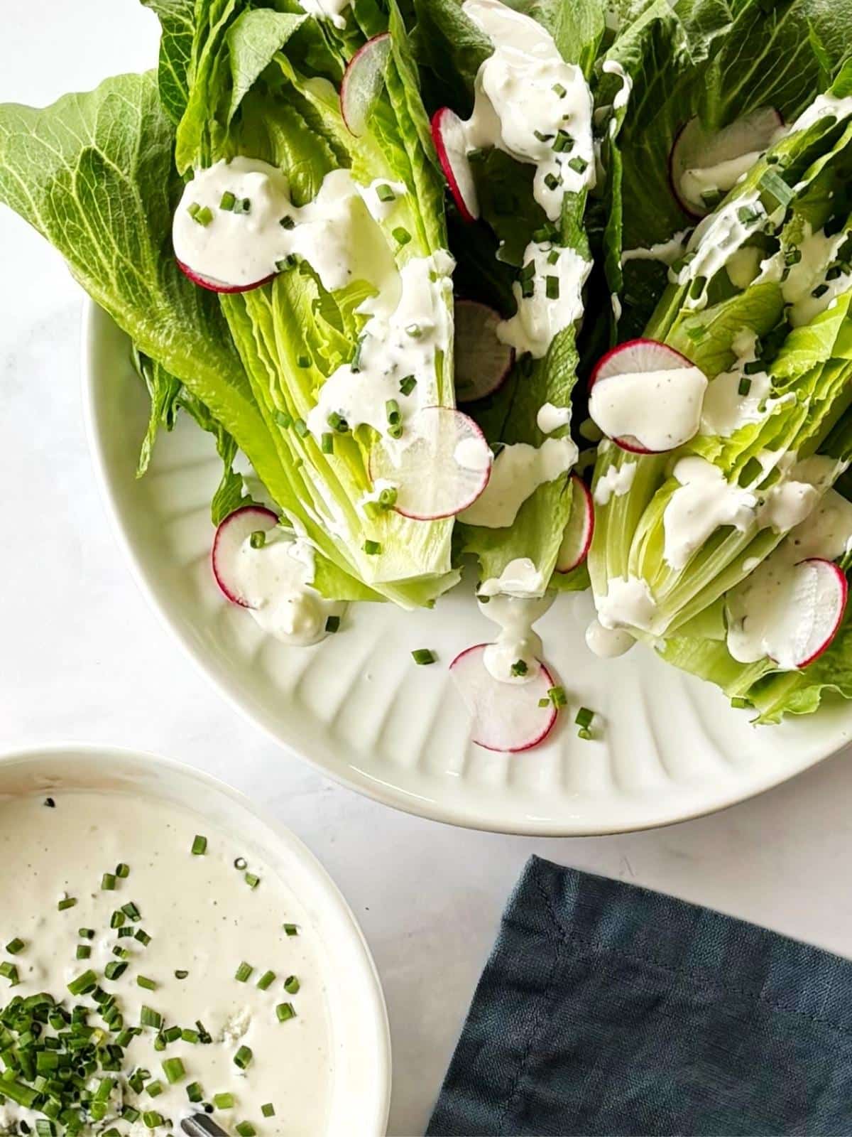 A plate of salad drizzled with dressing next to a bowl of blue cheese dressing.